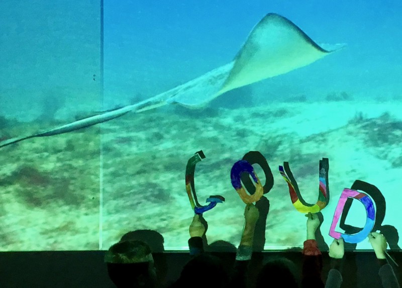 Kinderen houden letters omhoog in het blauwe licht van de projectie van een foto van aquarium met enorme vissen