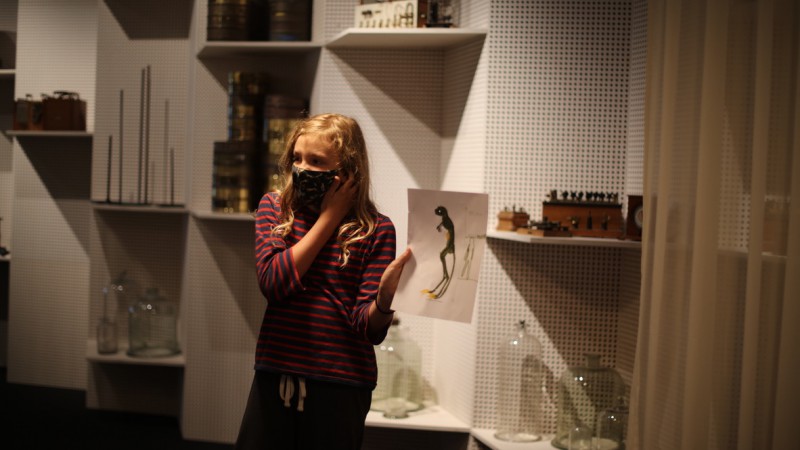 Meisje staat voor museumvitrine vol wetenschappelijke voorwerpen
