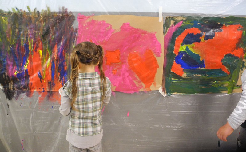 Petite fille paint avec beaucoup de couleurs sur une très grande feuille attaché au mur