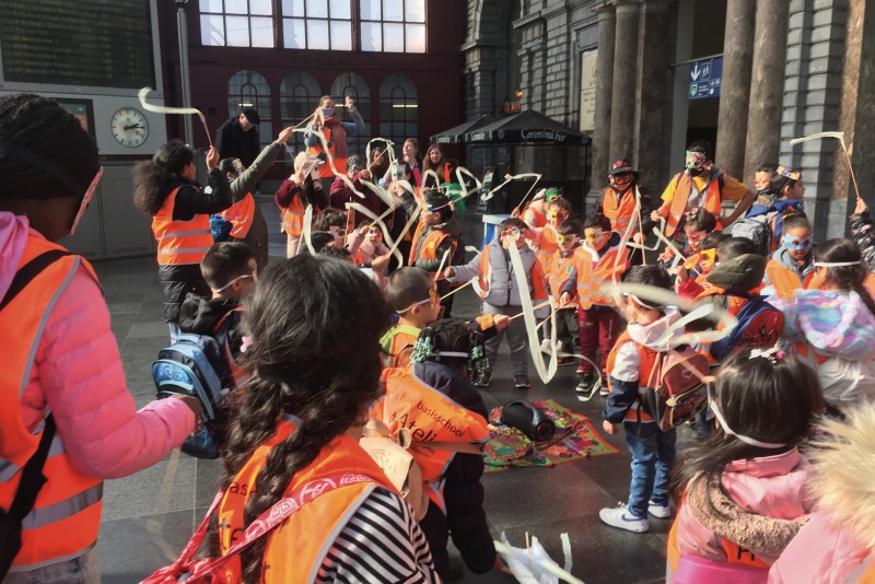 groupe d'enfants agitant des bâtons et des rubans dans le hall d'entrée de la gare centrale d'Anvers.