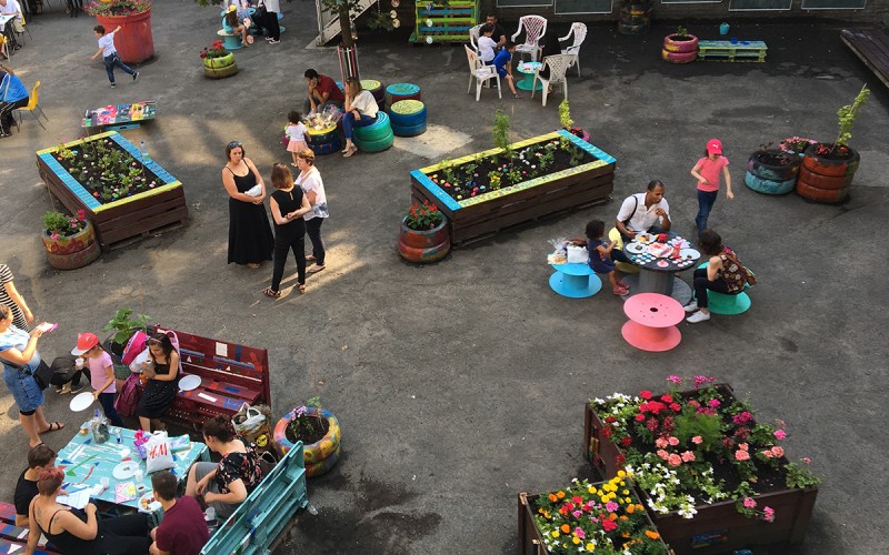 Fête d'école, dehors. Les parents se baladent parmi les installations colorés que Boris a fabriqués avec les enfants.